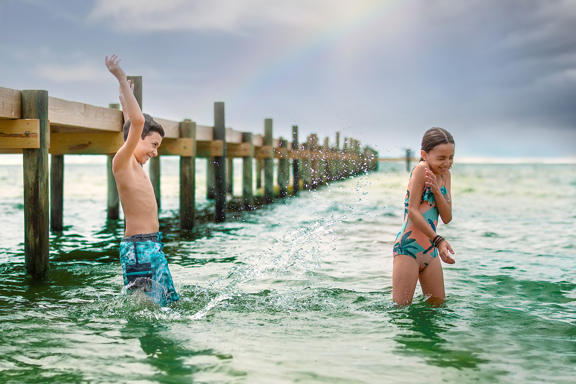 Boy and girl splashing water with a wooden pier in the background