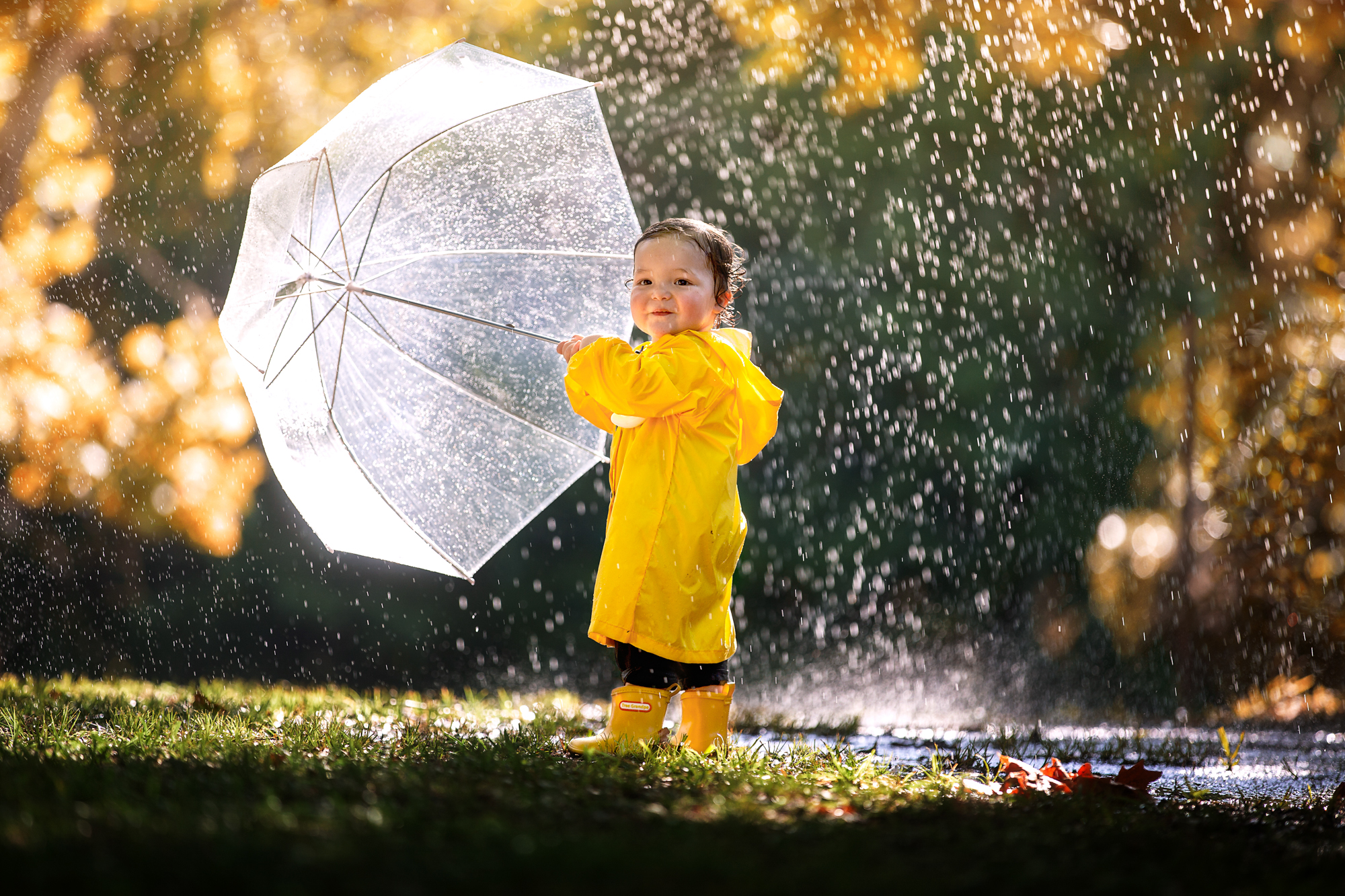 Little boy wearing a yellow raincoat while holding a clear umbrella under the pouring rain in Houston, Texas