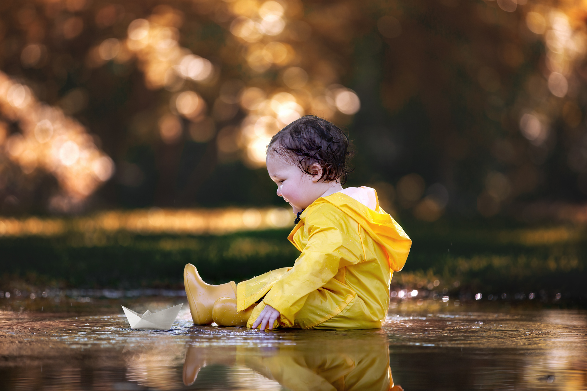 Adorable little boy playing with a paper boat while sitting on a puddle at the Discovery Green park in Houston, TX.