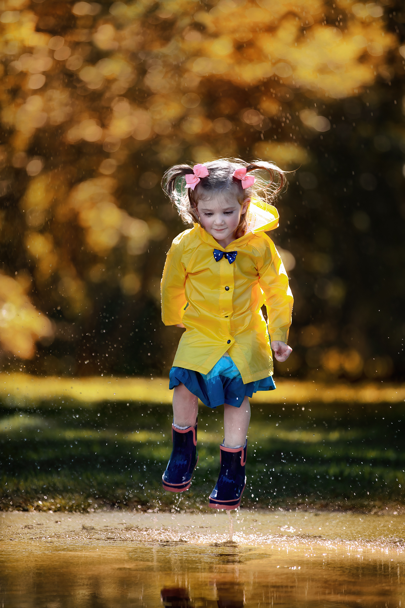 Beautiful toddler jumping on a puddle wearing rain boots and a rain coat.