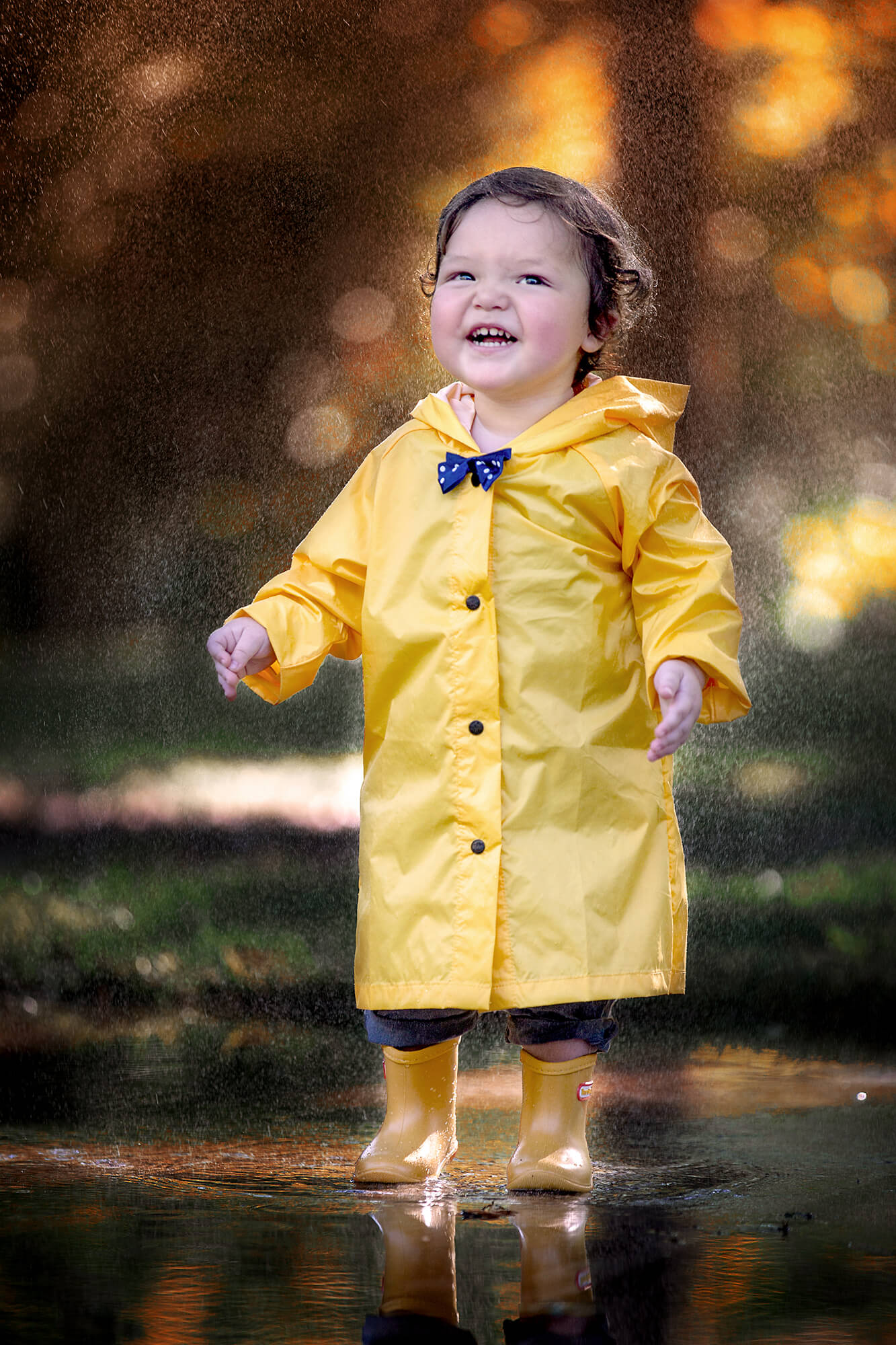 Adorable toddler boy playing in the rain in Houston wearing a bright yellow raincoat and rain boots
