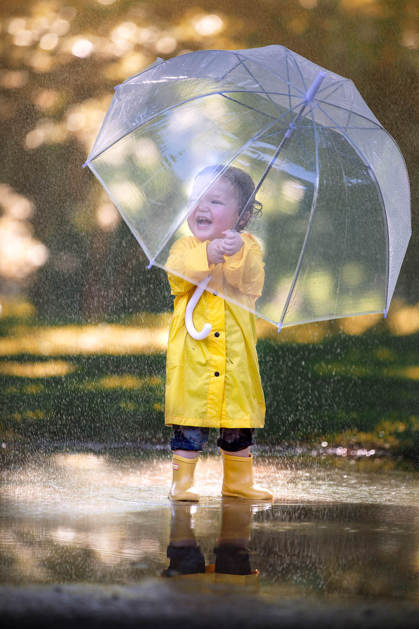Sweet toddler wearing a yellow raincoat and holding a clear umbrella bought at Baby Depot Houston.