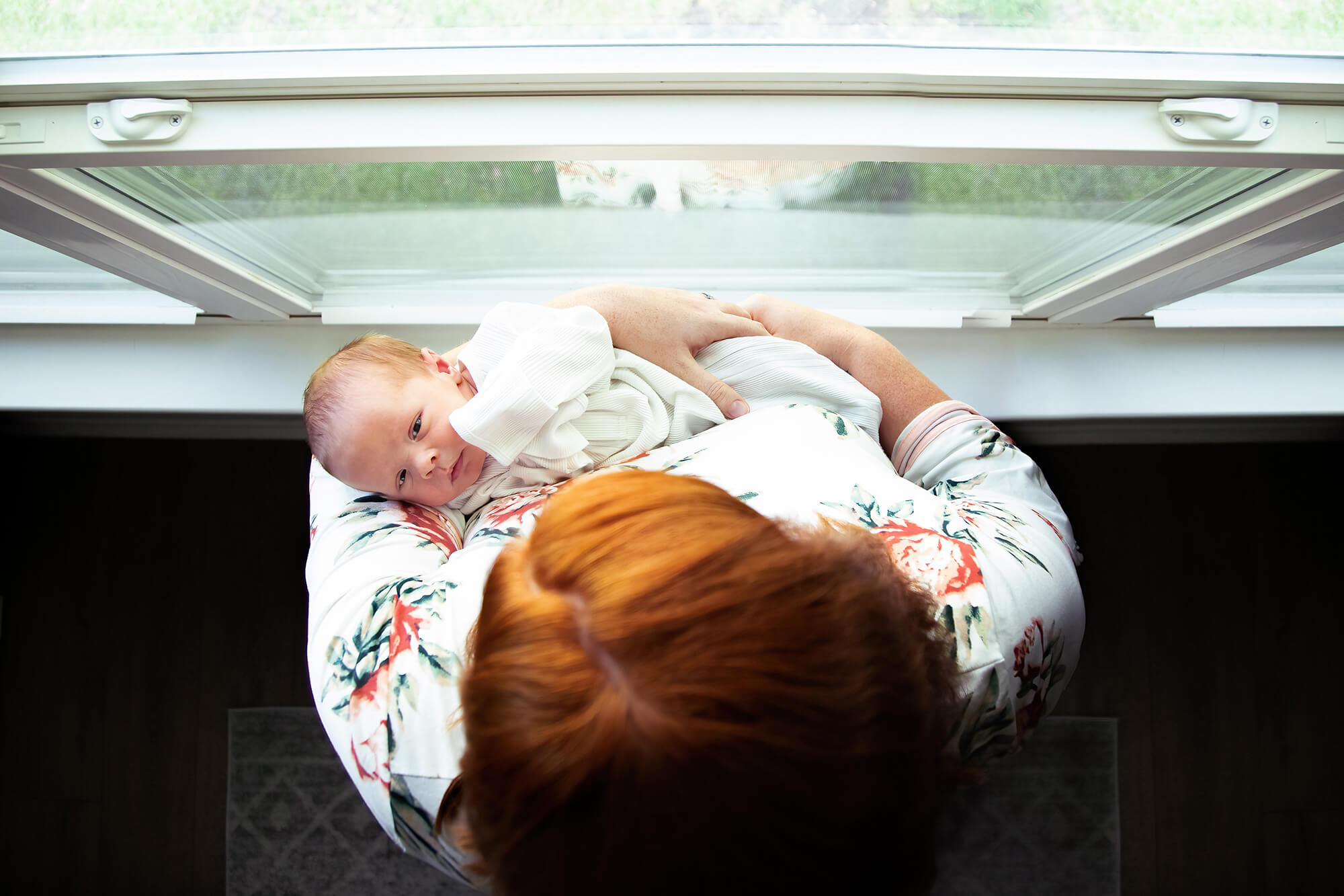 Red haired mom holding her newborn close to a window on the waiting room of Blue Fish Pediatrics