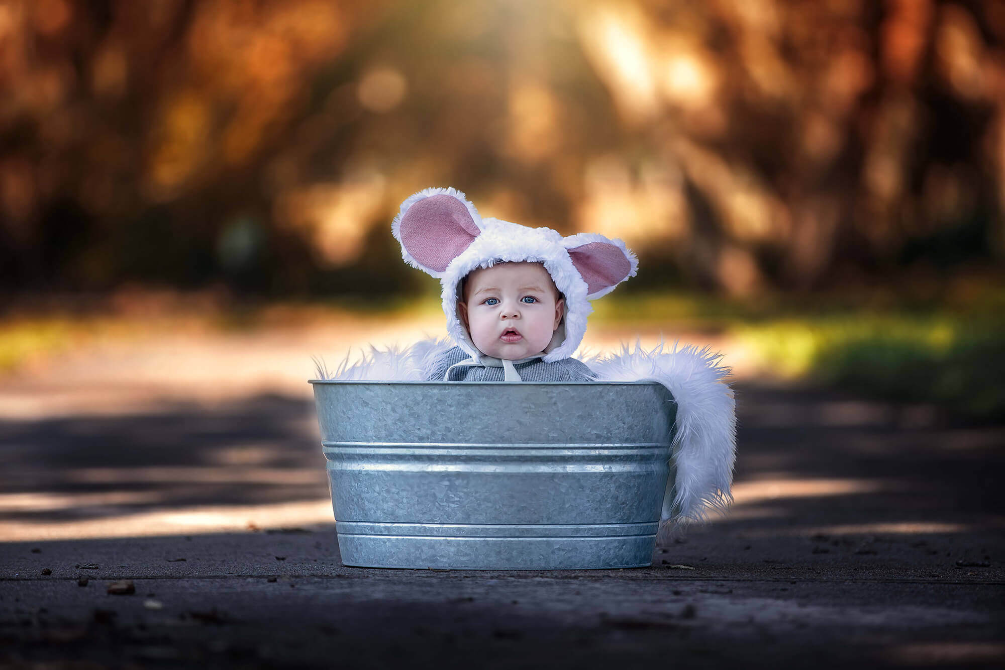 Adorable baby sitting inside a metal tub wearing a mouse bonnet from Kid to Kid Houston