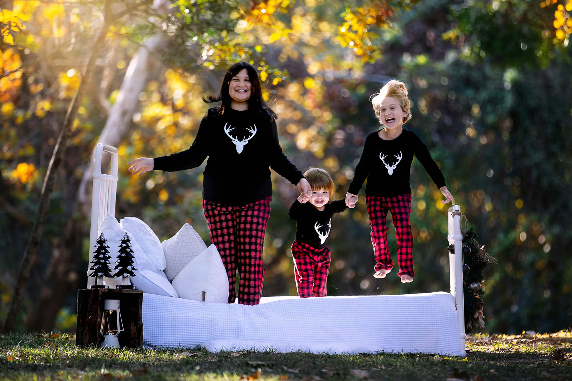 Three sisters wearing Christmas pajamas jumping on a bed excited to see Christmas lights in Houston.