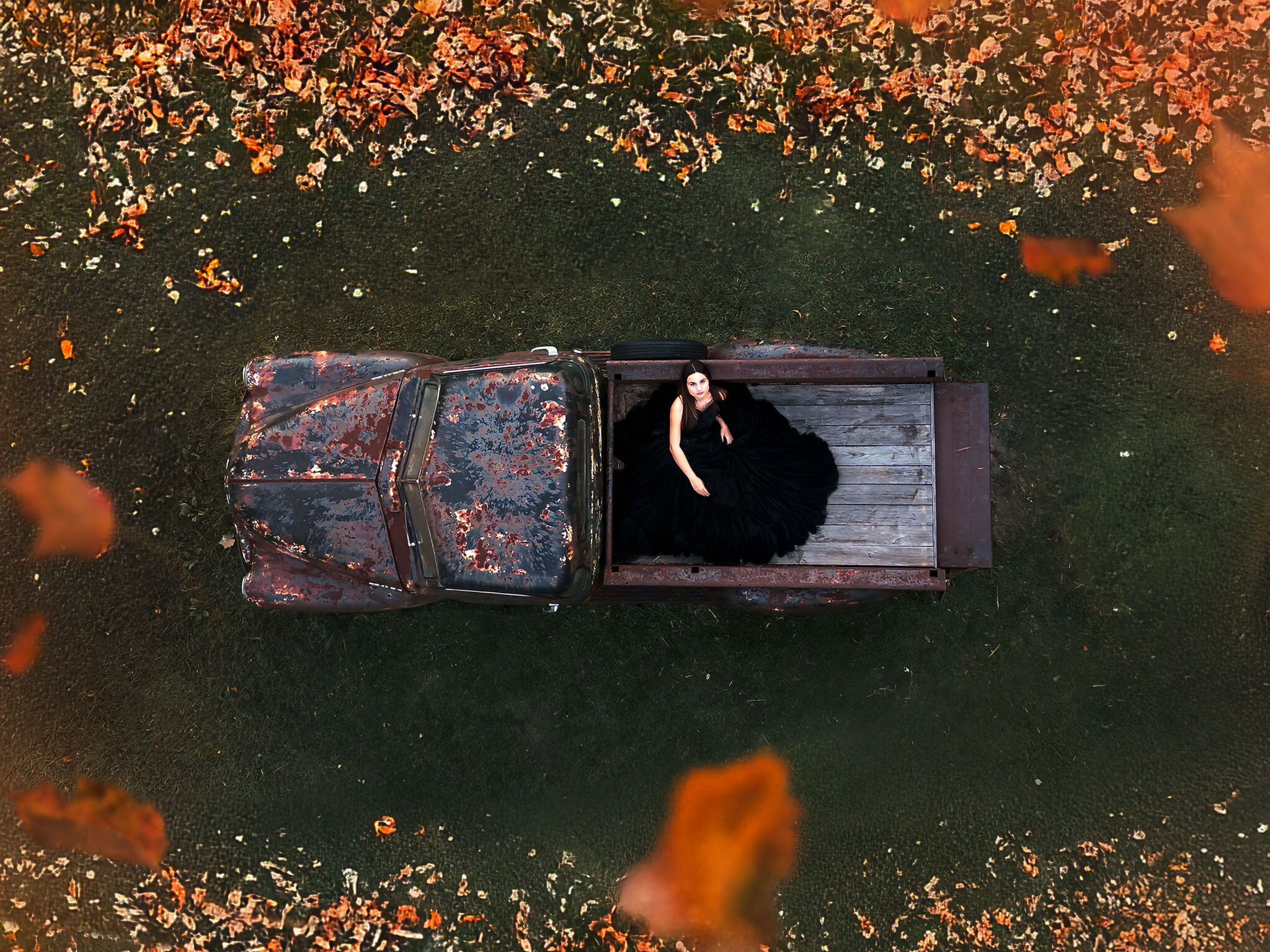 Girl wearing black dress sitting on the bed of a vintage truck surrounded by autumn leaves in Houston, Texas.